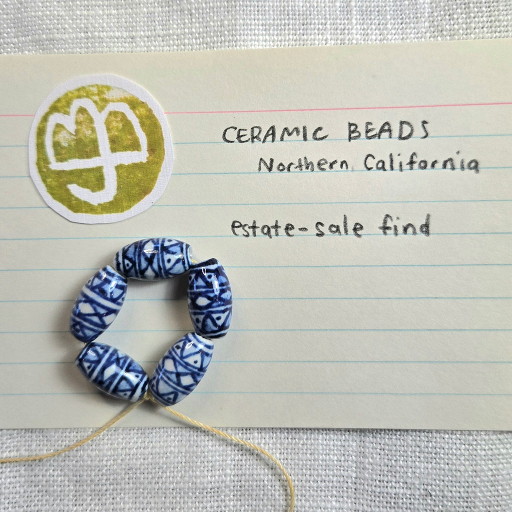 Five blue and white patterned ceramic beads arranged in a circle on a piece of lined notebook paper with handwritten text reading 'CERAMIC BEADS Northern California Estate-sale find'.