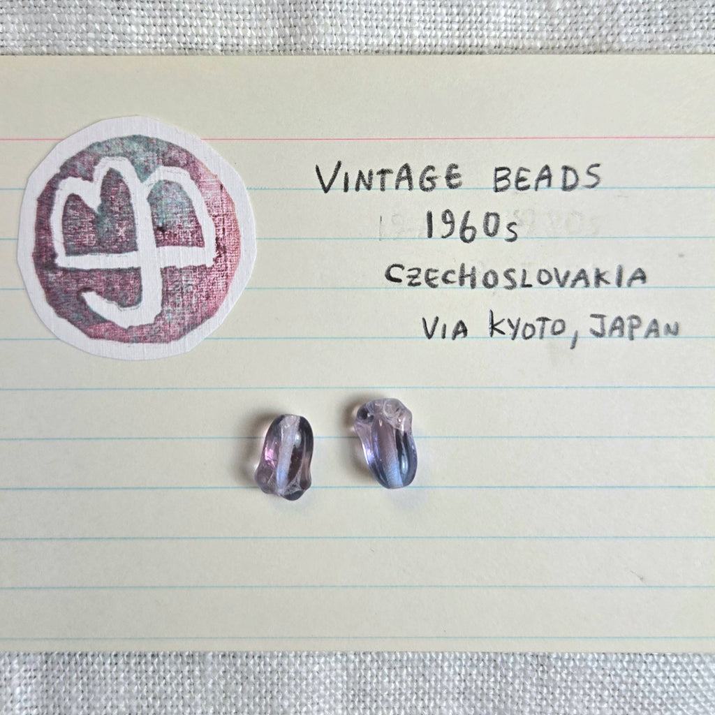 Two small vintage Czechoslovakia beads from the 1960s displayed on a lined notebook page next to a handwritten note and a logo.